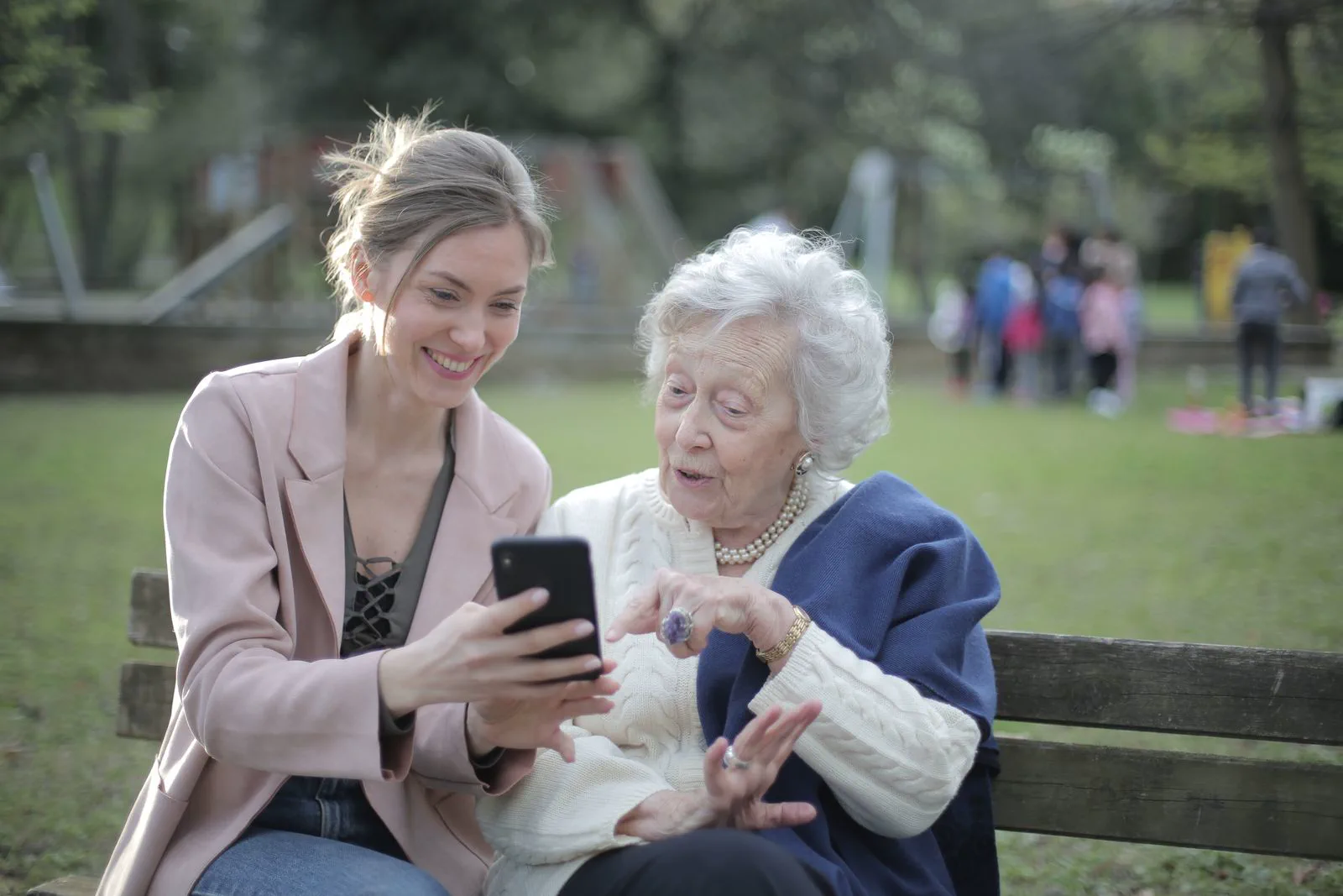 A daughter and her mother looking at a phone together on a park bench.