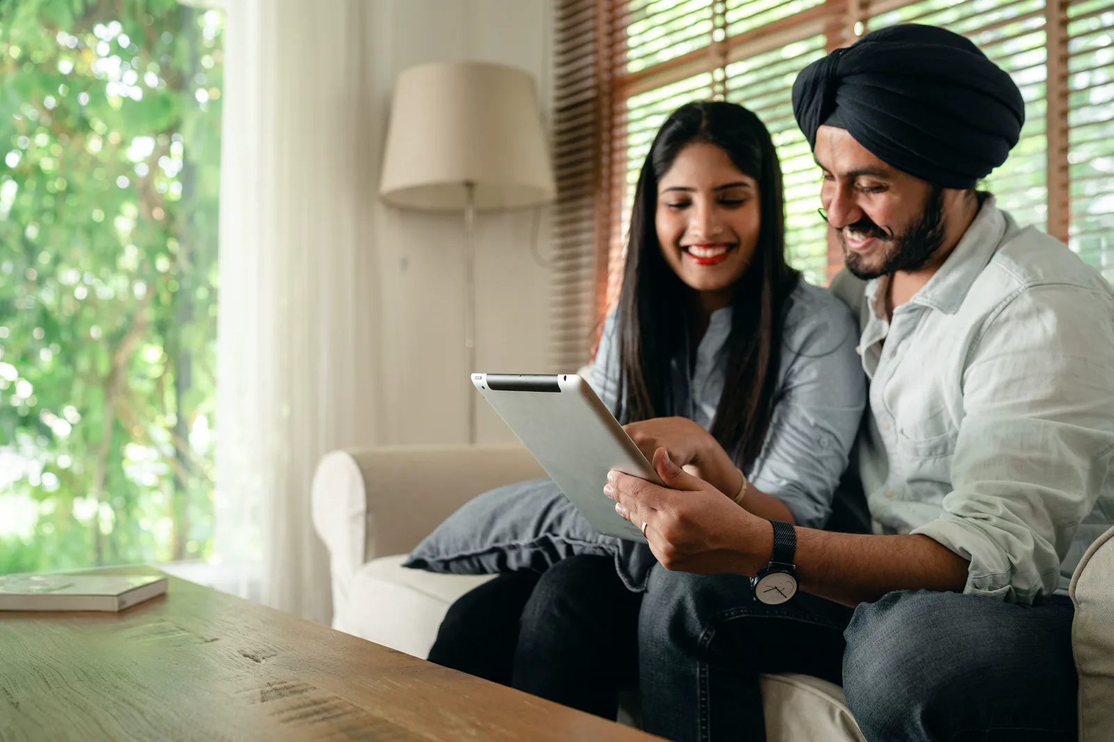 An Indian couple sitting together at home, smiling as they look at a tablet.